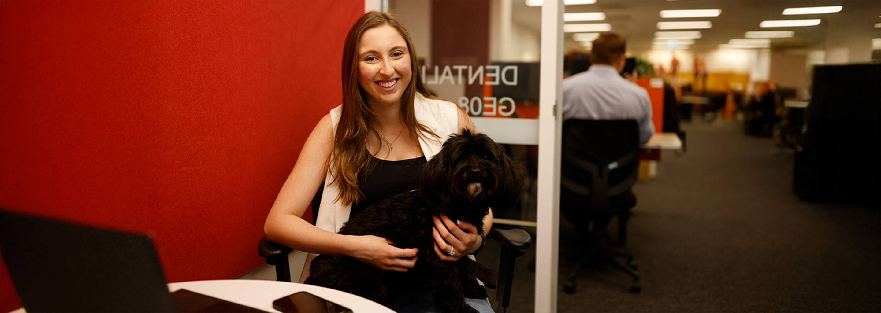 A smiling woman holding a fluffy black dog in an office.